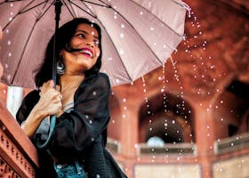 A cheerful woman with an umbrella enjoys the rain in New Delhi's architectural beauty.