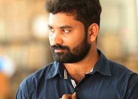 A thoughtful man with a beard and blue shirt posing indoors, displaying a stylish watch.